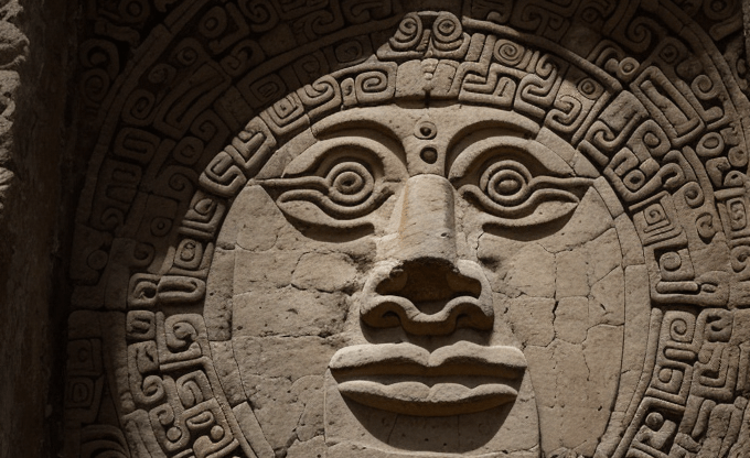 Письменность цивилизации Майя Рельеф с лицом, окруженным геометрическим узором, на каменной стене.